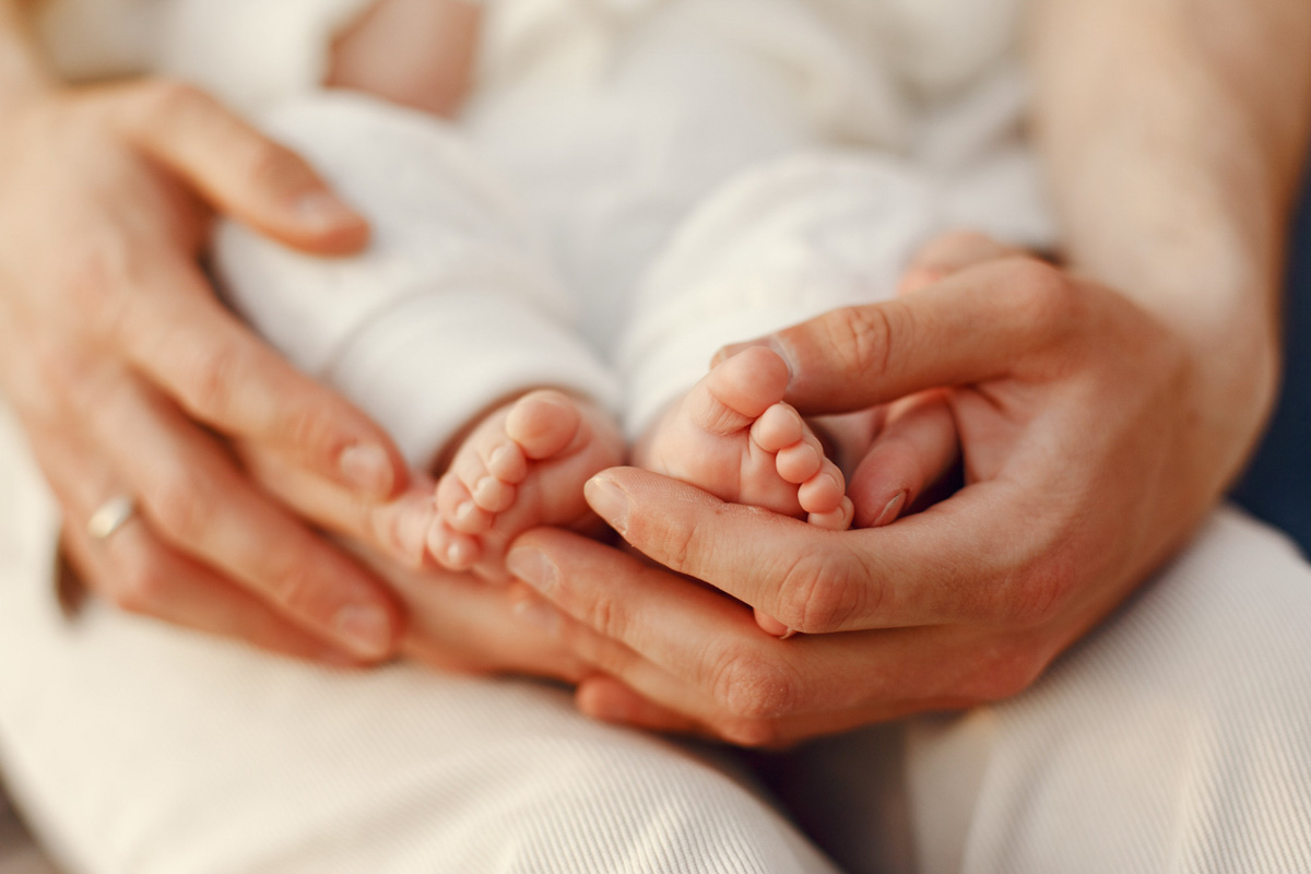 Erwachsene Hände halten sanft die kleinen Füße eines Babys